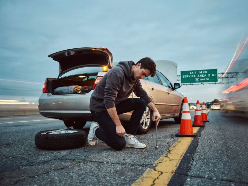 osoba wymieniająca koło na autostradzie